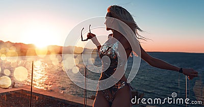 Girl in a beautiful bathing suit at sunset by the sea holding sunglasses Stock Photo