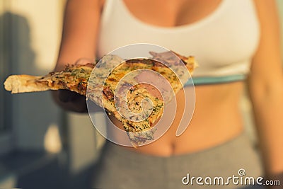 A girl with a beautiful breast in a sports suit holds a big piece of pizza in her hand Stock Photo