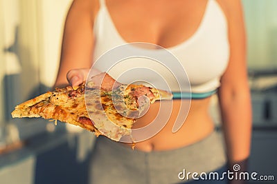 A girl with a beautiful breast in a sports suit holds a big piece of pizza in her hand Stock Photo