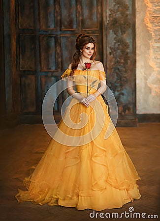 Girl beauty fantasy princess in yellow long historical, medieval silk dress holding flower red rose in her hands Stock Photo