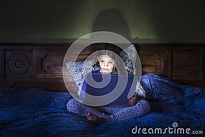 Girl in bed with laptop, glowing light. Stock Photo