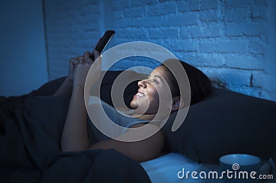 Girl in bed using mobile phone late at night at dark bedroom lying happy and relaxed Stock Photo