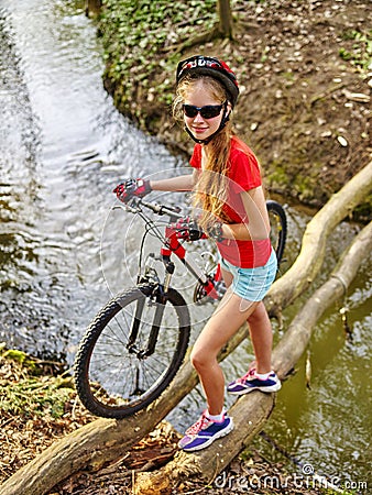 Girl on bicycle fording throught water on log . Stock Photo