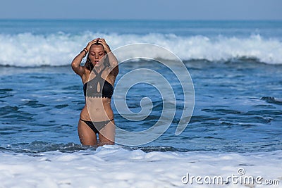 Attractive slim girl in black swimsuit coming out of the sea Stock Photo