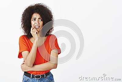 Girl biting nails from nervousness. Portrait of anxious insecure attractive female with afro hairstyle, holding finger Stock Photo