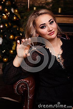 Girl in a black dress with scissors in her hands. preparation for the new year, christmas. hairstyle. tidy yourself up. Stock Photo
