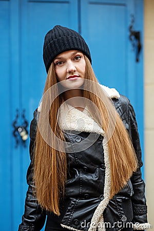 A girl in a black hat and a black jacket against a blue wall, stylish and youthful Stock Photo