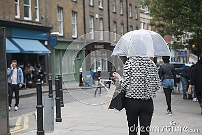 A girl in a black and white plaid fashion jacket under a transparent umbrella against the backdrop of London Editorial Stock Photo