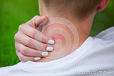 Girl with blond hair, sitting with his back turned and scratching bitten, red, swollen neck skin from mosquito bites in the summer Stock Photo