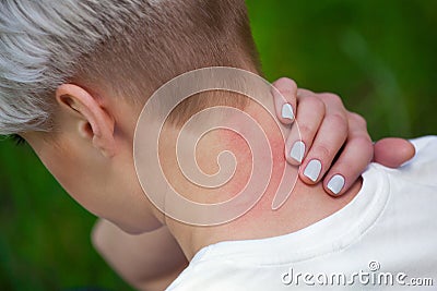 Girl with blond hair, sitting with his back turned and scratching bitten, red, swollen neck skin from mosquito bites Stock Photo