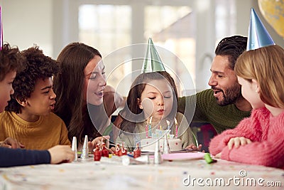 Girl Blowing Out Candles On Birthday Cake At Party With Parents And Friends At Home Stock Photo