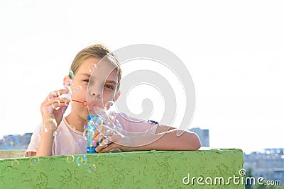 The girl blows bubbles on the balcony of a high-rise building, and looked into the frame Stock Photo