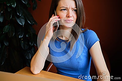 A girl in a blue dress sits at a cafe and swears on the phone Stock Photo