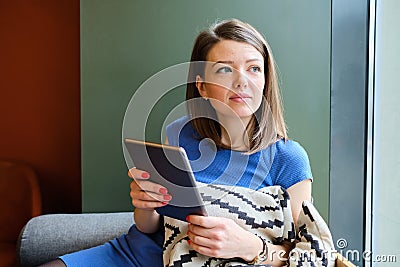 A girl in a blue dress sits at a cafe with a tablet and dreams Stock Photo