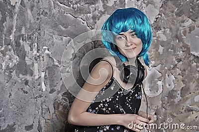 Girl in blue wig smiling with headphones on cement wall Stock Photo