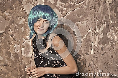 Girl in blue wig smiling with headphones on cement wall Stock Photo