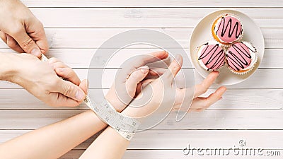 A girl with bound hands measuring tape reaches for a delicious sweetness.male hands holding a measuring tape without letting it Stock Photo