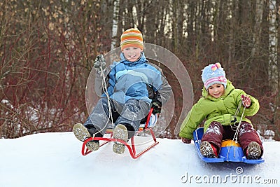 Girl and boy go downward from hill on sledges Stock Photo