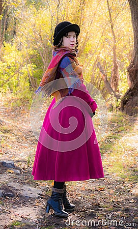 Girl in a bright crimson coat walking in forest sunny autumn day Stock Photo