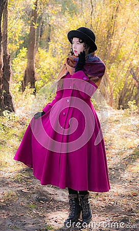 Girl in a bright crimson coat walking in forest sunny autumn day Stock Photo