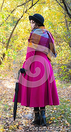 Girl in a bright crimson coat walking in forest sunny autumn day Stock Photo