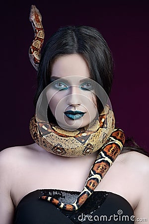 girl brunette green make up eyes gaze close up portrait with a snake yellow brown mottled python on a black pink background Stock Photo