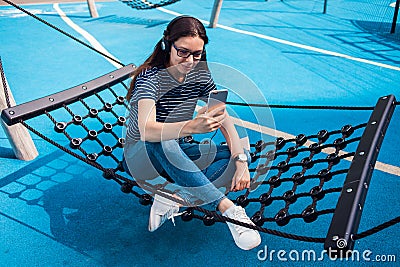 Girl, a brunette, sits in a hammock, sways, listening to music, dancing, relaxing, singing, trying to catch a wifi. Stock Photo