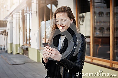 Girl is calling taxi. Beautiful modern woman in trendy clothes holding smartphone and looking at screen while messaging Stock Photo