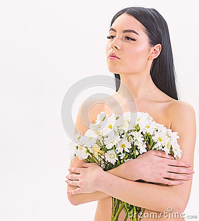 Girl on calm face naked holds chamomile flowers in front of breasts. Woman with smooth healthy skin looks attractive Stock Photo