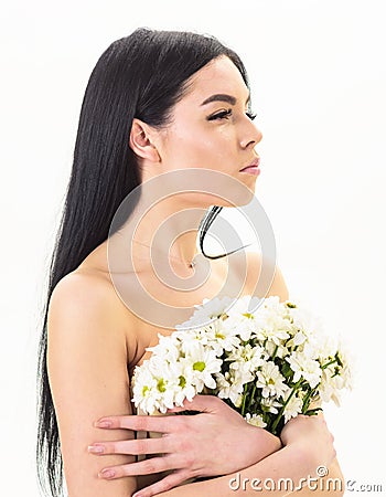 Girl on calm face stands naked and holds chamomile flowers in front of chest. Skin health concept. Lady covers breasts Stock Photo