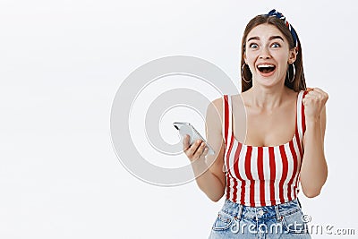Girl cannot believe miracle happened being surprised and happy clenching fist in success and victory holding smartphone Stock Photo
