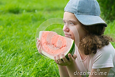 Girl in a cap, lies on green grass and holds a piece of watermelon, there is a place for inscription, close-up Stock Photo