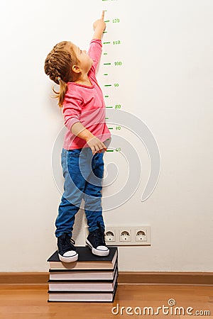 Girl checking height on growth chart at four books Stock Photo