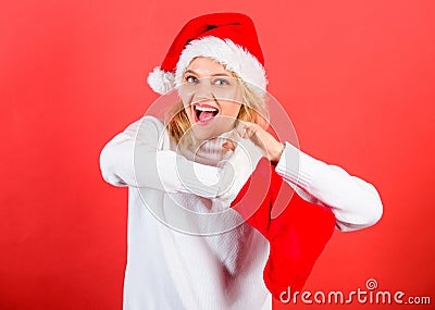 Girl cheerful face check out gift in christmas sock. Woman in santa hat unpacking christmas gift red background. Check Stock Photo
