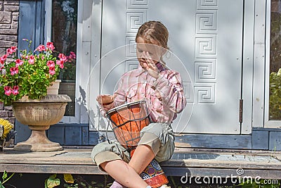 The girl child with a djembe drum outdoor on the porch of the house photo without processing Stock Photo