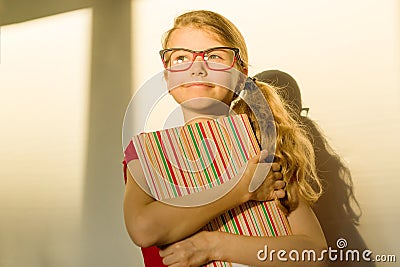 Girl child elementary school student wearing glasses is holding a textbook and dreamily smiling looking forward Stock Photo