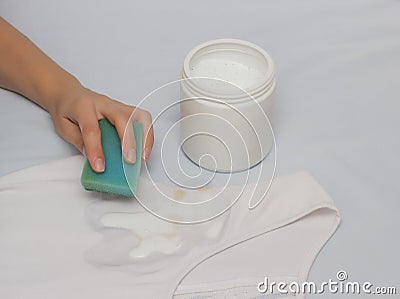 A girl cleans a stain with a sponge on a T-shirt using a stain remover, close-up, hand Stock Photo