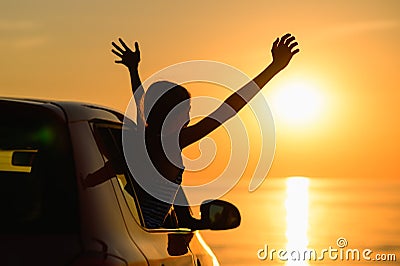 The girl climbed out of the car window with two hands up and looks at the beautiful sunset. Stock Photo