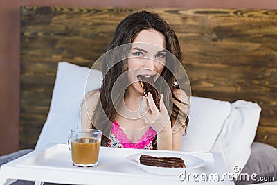 Girl with coffee in bed eating a cake Stock Photo