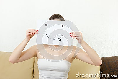 Girl cover her face with joyful teasing smile drawn on paper. Stock Photo