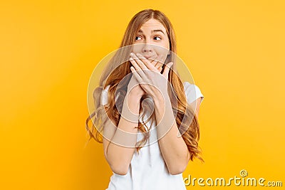 Girl covered her mouth with both hands, woman shocked on a yellow background, concept of silence Stock Photo