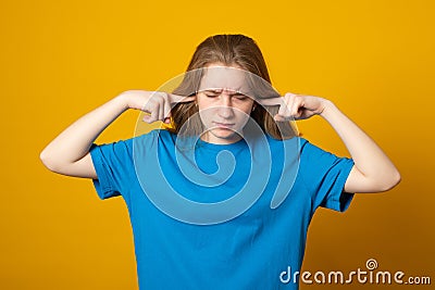 Girl covering her ears with hands for not to hear anything. Photo of young girl dressed in casual clothes on yellow background Stock Photo