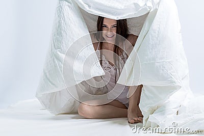 The girl crawled under the white blanket. Sit on bed after waking up. Fooling around. Stock Photo