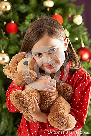 Girl Cuddling Bear In Front Of Christmas Tree Stock Photo