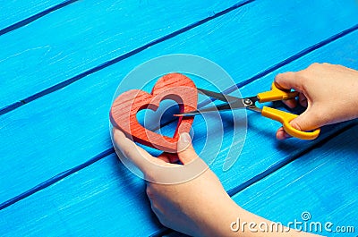 Girl cuts the heart with scissors, the concept of breaking relations, quarrels and divorce. Betrayal of the othere. blue backgroun Stock Photo