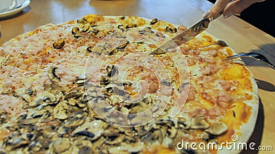 The girl cuts pizza with ham and mushrooms. Hands close-up. Stock Photo
