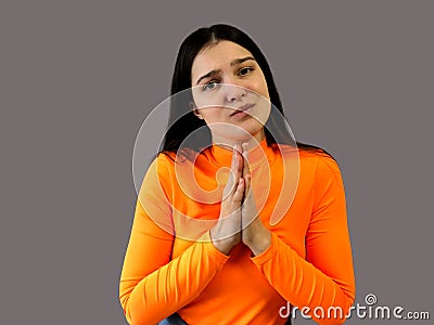 Girl with dark hair in a bright orange sweater on a gray background. implore Stock Photo