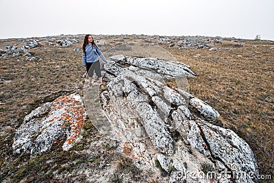 A girl with dark long hair in a marine vest stands at the huge stones sticking out of the ground. Stock Photo