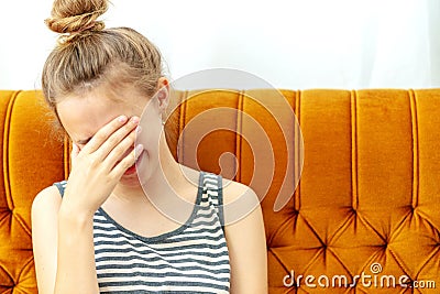 Girl in despair covers her face with hands sitting on a white sofa. Stock Photo