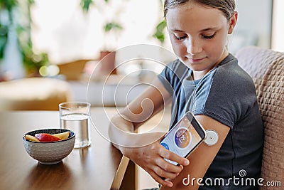 Girl with diabetes checking blood glucose level at home using continuous glucose monitor. Schoolgirl connecting CGM to Stock Photo